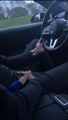 two people are sitting in the driver's seat of a car, both holding their hands on the steering wheel