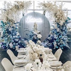 the table is set with white and blue flowers, plates, napkins and silverware