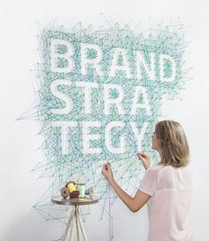 a woman is writing on the wall with white letters and green lines behind her that read brand strau tegov