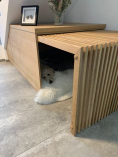 a white dog is laying down in a wooden cabinet under a table with flowers on it