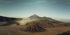 an aerial view of a mountain range with dust coming from the ground and clouds in the air