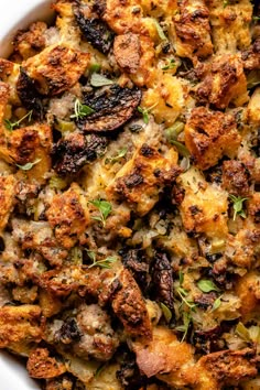 a casserole dish filled with stuffing and fresh herbs in a large white bowl