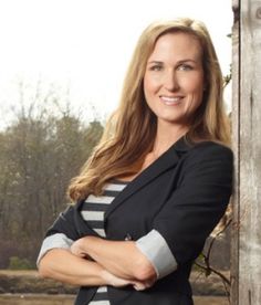 a woman standing in front of a wooden fence with her arms crossed and looking at the camera