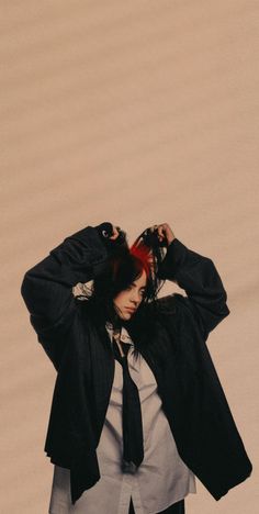 a woman wearing a suit and tie standing in front of a wall with her hands on her head