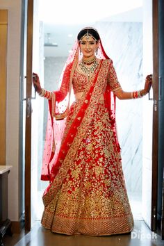 a woman in a red and gold bridal gown is standing on the door way