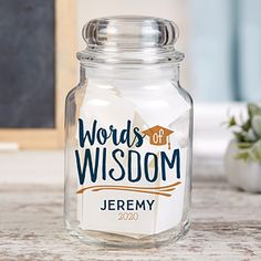 a glass jar sitting on top of a wooden table next to a chalkboard with the words words of wisdom