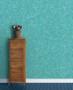 a vase with flowers sitting on top of a wooden cabinet in front of a blue wall