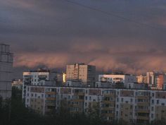 the city skyline is lit up at night with dark clouds in the sky above it