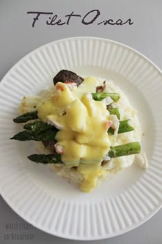 a white plate topped with mashed potatoes and asparagus covered in cheese sauce