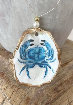 a blue crab on a white and gold plate is hanging from a silver necklace chain