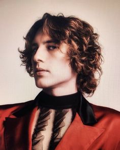 a young man with curly hair wearing a red jacket and black bow tie, looking to the side