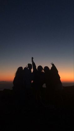 a group of people standing on top of a mountain at sunset with their arms in the air