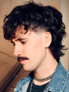 a man with a moustache on his face wearing a necklace and denim jacket