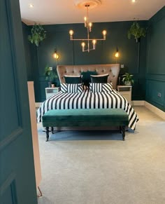 a bedroom with green walls and striped bedspread on the bed is lit by two lamps