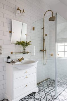 a white bathroom with black and white tile flooring, gold faucet, shower head, sink, and mirror