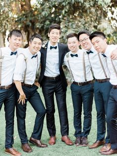 a group of men standing next to each other wearing suspenders and bow ties in front of trees