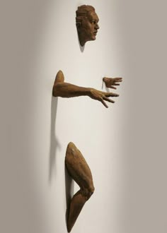 three wooden sculptures in the shape of hands and legs, hanging on a white wall