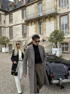 a man and woman walking next to an old car