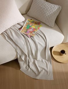 a white couch with a book on it next to some pillows and a spool of thread