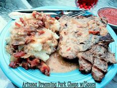 a blue plate topped with meat, potatoes and gravy next to a glass of wine