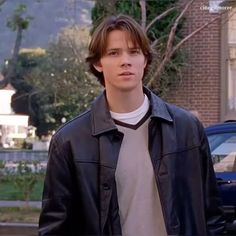 a young man standing in front of a building wearing a black leather jacket and white t - shirt