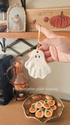 a hand holding a small ghost ornament next to a plate with cookies on it