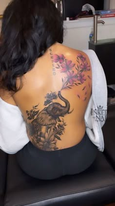 the back of a woman's body with an elephant and flowers tattoo on it