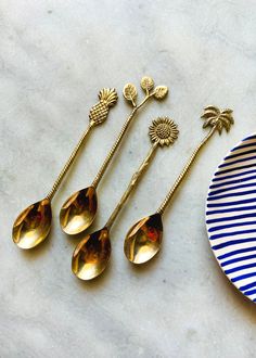 four golden spoons sitting on top of a white table next to a blue and white plate