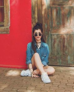 a woman sitting on the ground in front of a red wall with her legs crossed