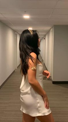 a woman in a short white dress is walking down the hallway with her hand on her hip