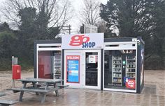 a small vending machine sitting next to a picnic table on a brick patio with trees in the background