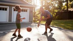 a father and son playing with a basketball on an asphalt court in front of a garage