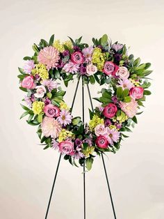 a pink and yellow wreath on a stand with green leaves in the center, surrounded by flowers