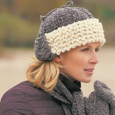 a woman wearing a knitted hat and mitten looks off to the side while standing in front of a body of water