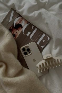 an iphone case sitting on top of a bed next to a hair comb and magazine