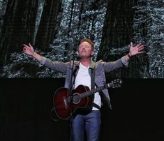 a man with his arms outstretched while holding a guitar in front of him and singing into a microphone