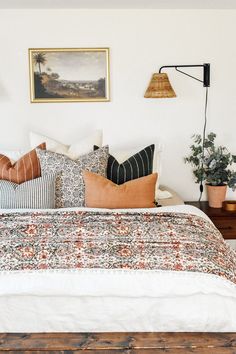 a bed with lots of pillows on top of it next to a lamp and potted plant