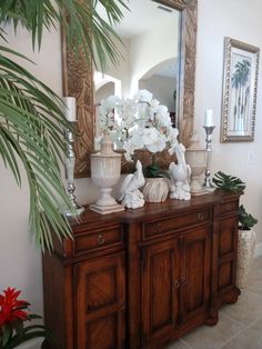 a large mirror sitting on top of a wooden cabinet next to a vase filled with flowers