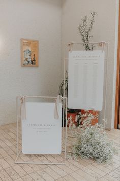 two white signs sitting next to each other on top of a tiled floor in front of a potted plant