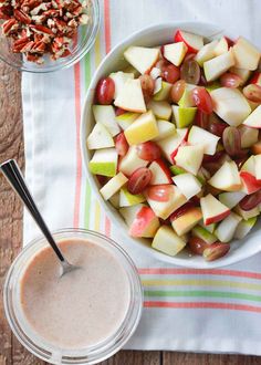 a bowl of apples, grapes and nuts next to a glass of milk