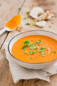 a white bowl filled with carrot soup on top of a wooden table