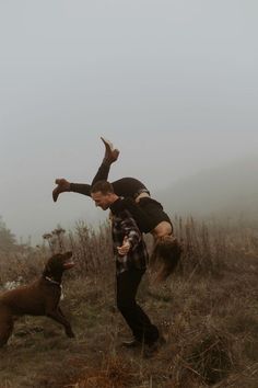 a man and his dog playing with each other in the grass on a foggy day