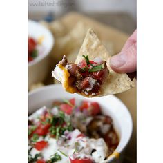 a hand holding a tortilla chip over a bowl of salsa