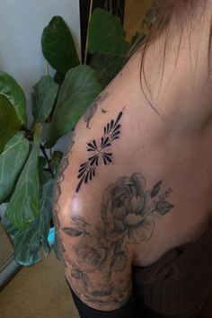 a woman with a flower tattoo on her arm and shoulder, next to a potted plant