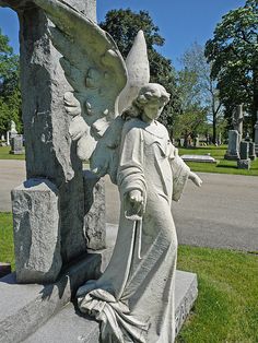 a statue of an angel holding a staff next to a stone cross in a cemetery