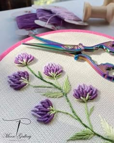 a pair of scissors sitting on top of a table next to purple flowers and needles