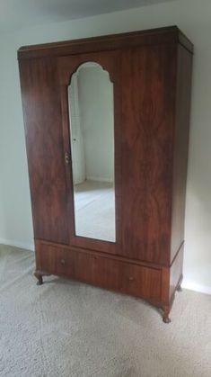 a large wooden armoire with a mirror on the front and bottom shelf, in an empty room