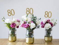 three mason jars with flowers in them and the number 80 on each one is gold