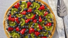 a pie topped with kiwis, blueberries and strawberries on top of a table