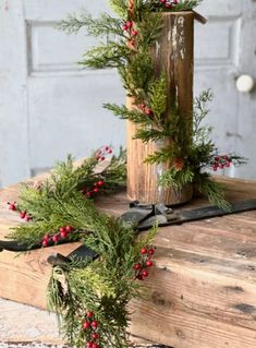 a wooden pole with evergreen and red berries on it next to a pair of scissors